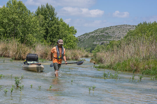 Angler Pulling Kayak Through Shallow River with Mountains