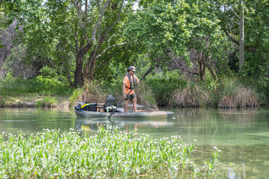 Hispanic Male Angler Standing in Fishing Kayak on Calm River