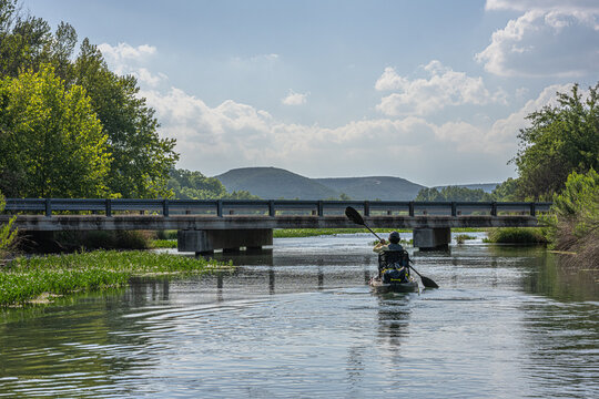 Angler Kayaking Toward Bridge on River with Mountain Vista