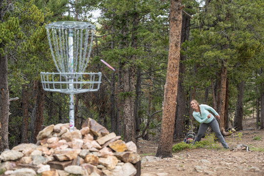 Caucasian Woman Throwing Disc Golf Frisbee Toward Basket in Forest