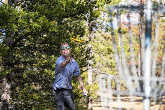 Man throwing disc toward basket during disc golf game in the woods