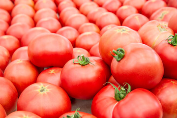 A dense pile of ripe, pinkish-red tomatoes, a few of which still have their fresh green stems.