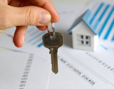 A professional real estate agent's hand is holding a key to a new house, giving a successful business partner the keys to a luxury property for a mortgage or rent deal