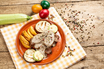 A plate of pork tenderloin medallions topped with a rich Roquefort cheese sauce, served with golden potato wedges and grilled eggplant.