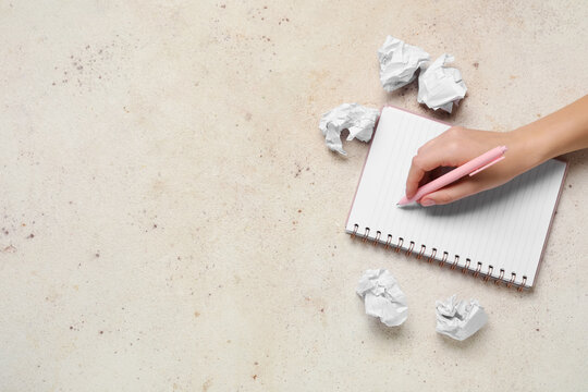 Female hand with notebook and crumpled pieces of paper on white grunge table