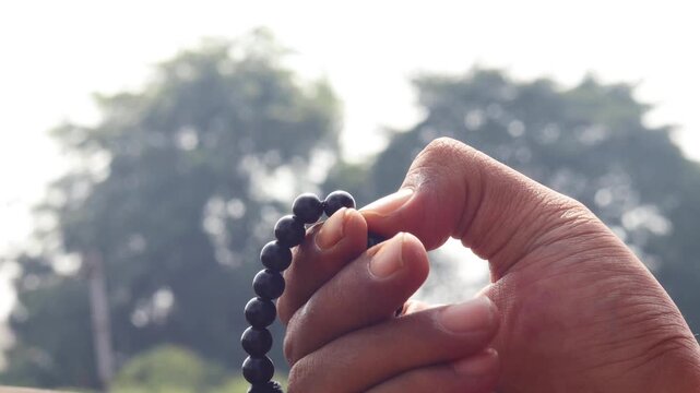 Close up of Asian man hands reciting dhikr using prayer beads against blurred background. Dzikir hand. spiritual devotion, meditation, faith practice, and religious reflection concept.