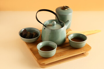 Fototapeta premium Tray with teapot, cups of tea and dry pressed puer leaves on color background