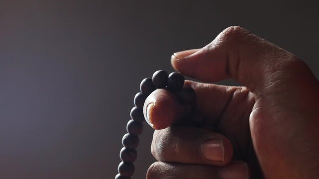 Close up of Asian man hands reciting dhikr using prayer beads against dark background. Dzikir hand. spiritual devotion, meditation, faith practice, and religious reflection concept.