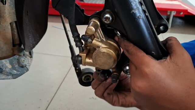 Close-up of vocational student repairing motorcycle disc brake caliper in automotive workshop. Hands adjusting brake components during practical mechanical training