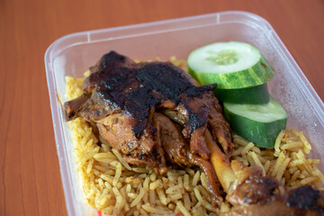 Flavorful Biryani Rice with Grilled Meat and Fresh Cucumber Slices in Plastic Container