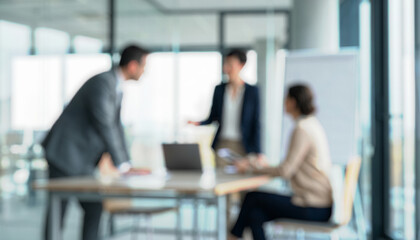 Blurry image of a business meeting in a modern office. Three professionals engaged in discussion over documents and laptop. Bright windows provide natural light.