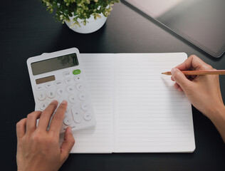 Financial planning concept with hands using calculator and writing in notebook on desk managing budget expense tracking accounting and personal finance organization.