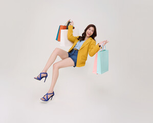 Shopping lifestyle concept with Asian woman holding colorful shopping bags floating mid air celebrating retail sale fashion spending and joyful consumer behavior in modern ecommerce culture.