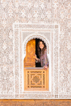 A woman smiles from a carved wooden window in an ornate, carved white wall. Madrasa di Ben Youssef,Marrakech,Morocco