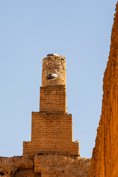 A stork stands on one leg atop a brick tower in Palais El Badi, with another stork nesting above, against a clear blue sky. Palais El Badi,Marrakech,Morocco