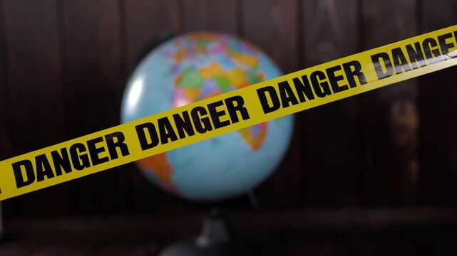 Close-up of a globe on a dark wooden background. In the foreground, there is a yellow warning tape with the inscription DANGER. World problems, ecology, and protection of the planet are discussed.