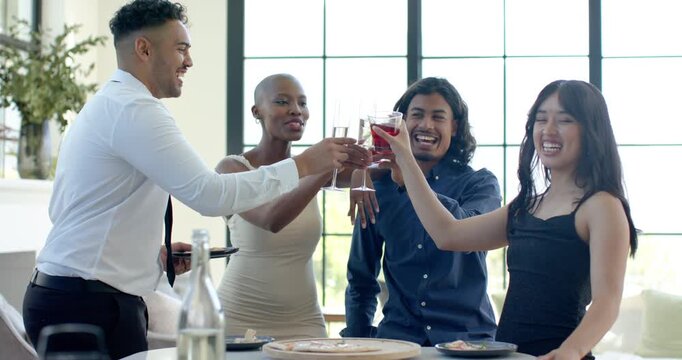 Diverse friends formally toasting with flutes and cups at living room table, man reaching to clink