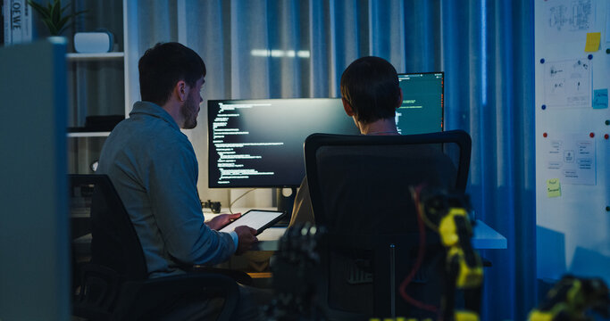Team adult male engineer collaborate on robotic hand project using AI code solutions machine learning at tech workspace night. Artificial intelligence interface, collaboration prototype development.