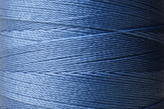 Macro close-up of a blue sewing thread spool with visible fiber texture and soft lighting. Minimalistic textile background representing tailoring, precision work, and creative craftsmanship.
