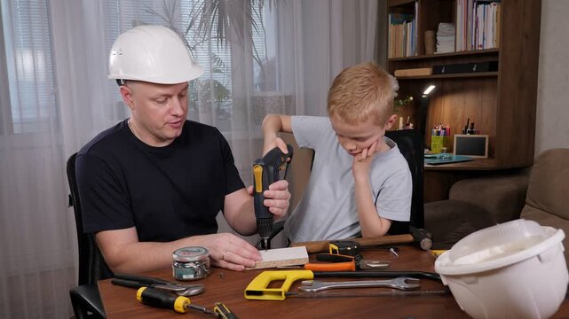 A loving and thoughtful father demonstrates various tools to his young son while they sit at the dining table at home. The father imparts knowledge to his son.