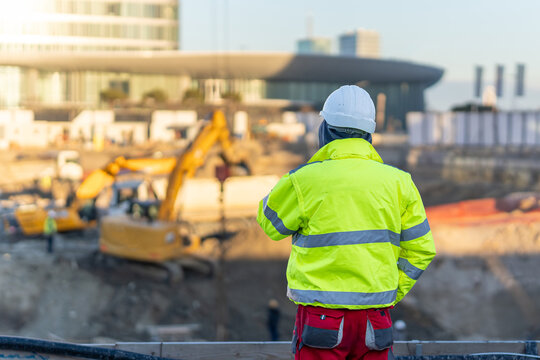 Construction worker in high visibility jacket and hard hat overseeing excavator at building site