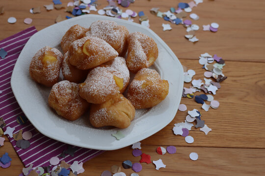 Traditional italian fritters filled with cream called Frittelle on a plate on wooden table with colorful paper Confetti decorations
