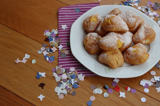 Traditional italian fritters filled with cream called Frittelle on a plate on wooden table with colorful paper Confetti decorations