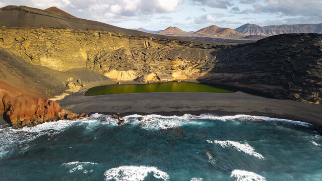 Aerial view of the contrasting vibrant green lagoon against the black volcanic rock, meeting the turquoise ocean waves, El Golfo, Lanzarote, Spain.
