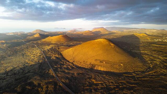 Aerial view of the volcanic cones bathed in the warm glow of the setting sun, creating a tapestry of light and shadow across the arid landscape, Lanzarote, Canarias, Spain.