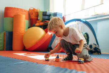 Toy cars, playing with them. Cute preschool child, boy, during developmental activities in a playroom