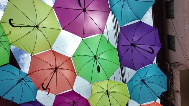 Vibrant upward view of dozens of colorful umbrellas suspended over the cobblestone Calle del Recuerdo street, forming a unique decorative canopy against the bright blue sky in Guatape, Colombia.