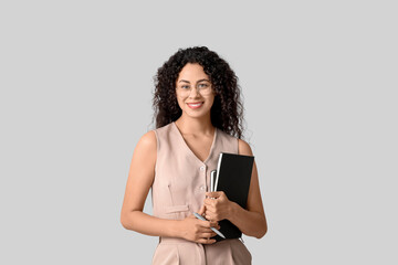 Fototapeta premium Young African-American businesswoman with notebooks on grey background