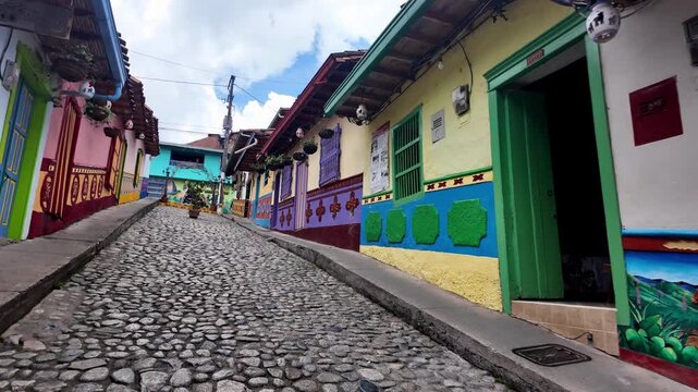 Experiential POV Moving Shot Walking Uphill on a Traditional Cobblestone Street Lined with Brightly Colored Z&oacute;calo Murals in Guatape, Colombia.