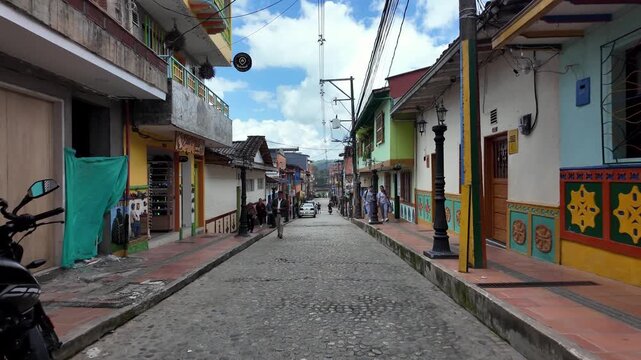 POV Moving Downhill View Along Bustling Commercial Street Lined With Colorful Z&oacute;calo Buildings in Guatape, Colombia.