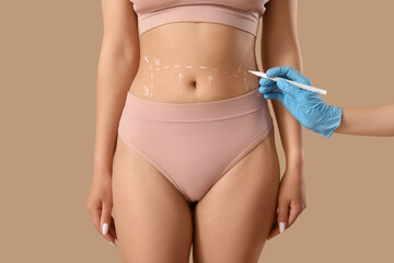 Plastic surgeon marking woman's belly on beige background, closeup
