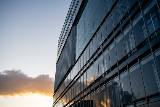 Modern corporate office facade in glass and steel capturing skyline reflection at sunset with urban architecture symmetry pattern and clean lines