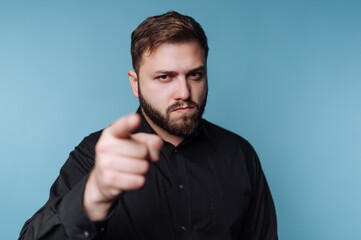 Obraz premium Confident man pointing directly at the viewer with a serious expression against a soft blue background