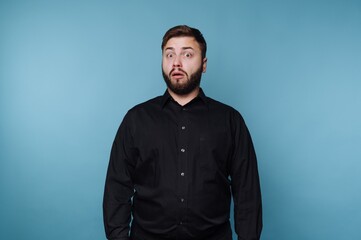 Obraz premium Expression of surprise captured in a modern studio setting with a blue backdrop featuring a man in a black shirt