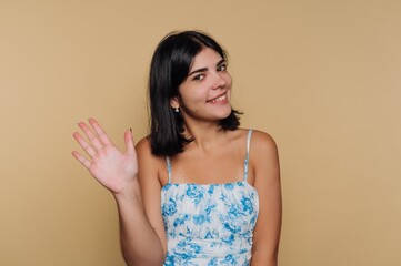 Obraz premium Smiling young woman waves cheerfully against a warm, neutral background during a sunny afternoon
