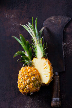 Sliced baby pineapple and old cleaver on rusty metal