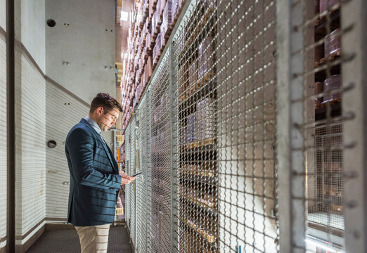 Man in automatized high rack warehouse looking at cell phone