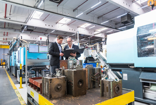 Two men with documents talking in factory shop floor