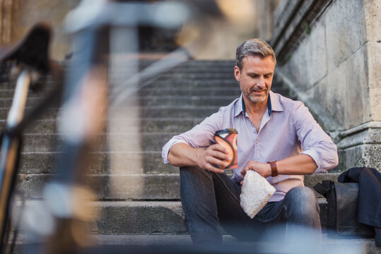 Man sitting on stairs with takeaway coffee in the city checking the time