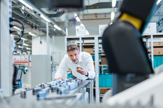 Businessman in a modern factory hall examiming workpieces