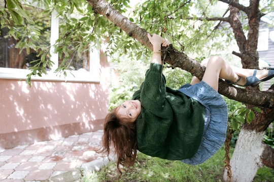 Cute girl hanging from tree branch in back yard