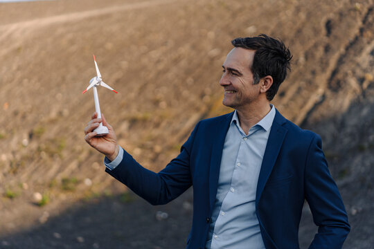 Happy mature businessman on a disused mine tip holding wind turbine model