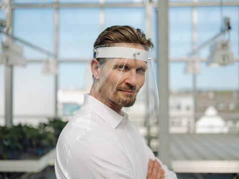 Close-up of businessman wearing face shield while working in greenhouse