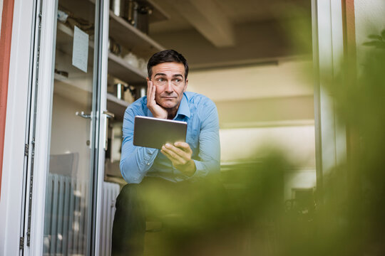Businessman with tablet sitting at open French door