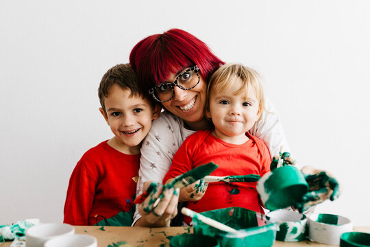 Mother with her children doing crafts at home and painting with green
