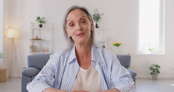 Senior woman looking at webcam having webinar or video call with family sitting in living room at home. Female person talking online indoors. Retirement and communication technology concept. 4k video